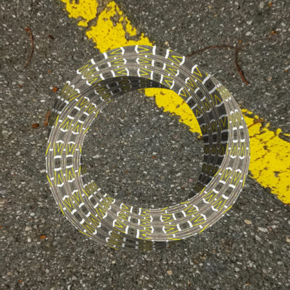 Dreidimensionales, zieseliges Möbiusband schwebt über einer Asphaltfläche. im Rechten oberen Eck des Bildes zieht sich ein gelber Markierungsstreifen 45 Grad winklig von links oben nach rechts unten