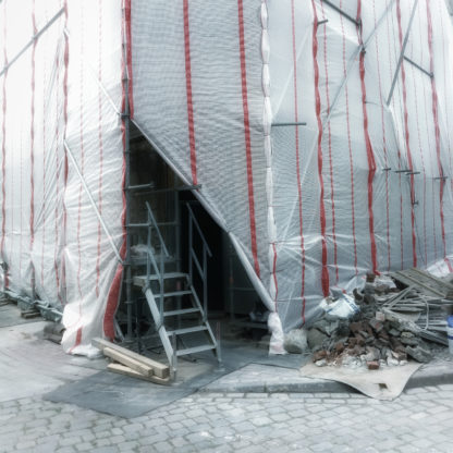Dreieckig bleckt der Eingang zu einem Baugerüst, verhangen von Plastikplanen. Eine Leiter führt ins Dunkel hinter den Planen der Gebäudeecke.