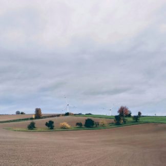 Pastellfarbene, noch kahle, herbstliche Agrarlandschaft, von einem Hügel aus betrachtet. Zwei Drittel des Bildes sind Himmel.
