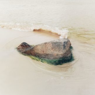 Zarte hautfarbene Strandszene eines koffergroßen Steins, der vom Meer umspült wird.