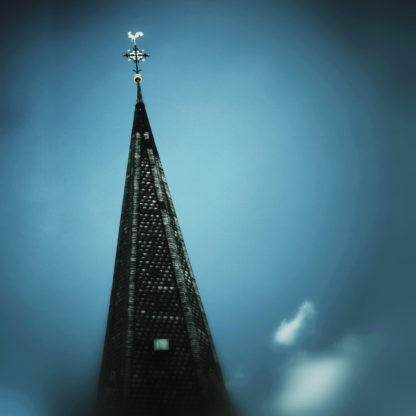 Die Spitze eines Kirchturms ragt bis fast zum oberen Bildrand in eine blaugrau düstere Athmosphäre. Der Hahn schimmert.