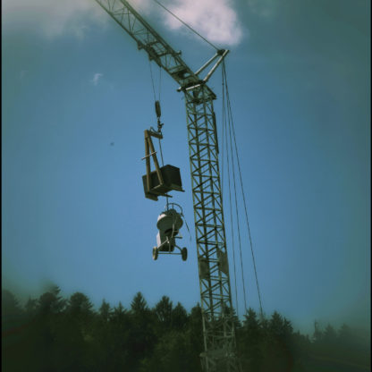 Am Arm eines Baukrans hängen Maschinen über dem Wald im Hintergrund
