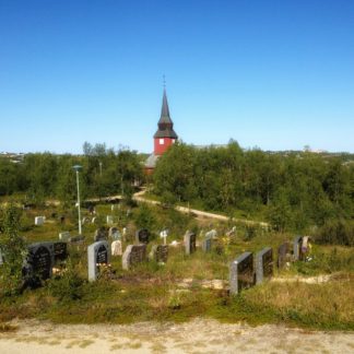 Über einen Friedhof zwischen Grabsteinen bahnt sich dein Blick den Weg durch geducktes Gesträuch, dem man die arktische Kargheit anmerkt. Am Horizont unter blauem Himmel ragt fern ein roter Kirchturm aus dem Grün