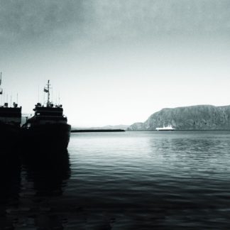 Schwarzweiß-Bild eines Hafens im Gegenlicht. Links liegt ein Schattenriss eines Schiffs. Im Hintergung öffnet sich eine Meeresbucht, die von gegenüberliegenden Bergen gerahmt wird