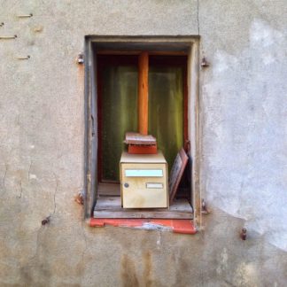 Ein Briefkasten in einer Fensteröffnung, auf dem ein Kantholz verkeilt ist