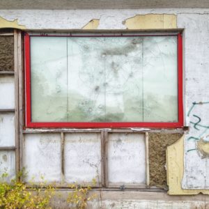 Zerfallende Fassade mit einem alten, rot umrandeten Schaufenster, das durch eine Bretterwand ersetzt wurde