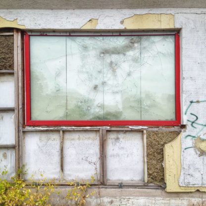 Zerfallende Fassade mit einem alten, rot umrandeten Schaufenster, das durch eine Bretterwand ersetzt wurde