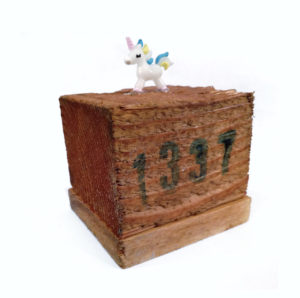 Winzige Einhornfigur aus Kunststoff auf einem Sockel, der einmal als Fuß einer Europalette diente. Auf dem hölzernen Kubus ist in grünlich-schwarzer Schrift relativ unsauber die Zahl 1337 gedruckt.